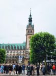 Menschen treffen sich vor dem Rathaus Hamburg, man erkennt den schönen Turm, es wirkt regnerisch.