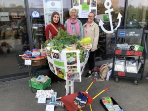 Drei Frauen lächeln in die Kamera. Sie stehen vor einem Drogeriemarkt der Kette Budni und ein Stehtisch ist u.a. mit Grünzeug geschmückt.