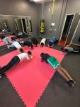 Acht männliche Jugendliche machen Unterarmstütz in einer Art Fitness-Raum, im Hintergrund u.a. ein großer Wand-Spiegel und ein Boxsack von der Decke