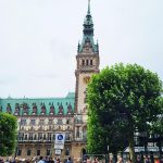 Menschen treffen sich vor dem Rathaus Hamburg, man erkennt den schönen Turm, es wirkt regnerisch.