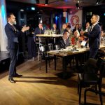 Zwei Männer stehen sich mit einem Abstand von circa 2 Metern gegenüber, konzentrieren sich auf "irgendwas". Dahinter und daneben sitzendes Publikum