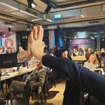 Ein Mann und eine Frau führen ihre Handflächen zusammen, im Hintergrund Publikum.