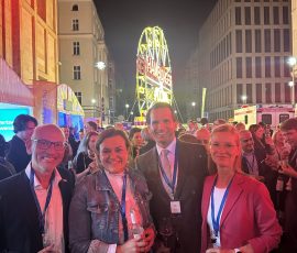 4 lächelnde Menschen vor einer Menschenmenge vor einem Riesenrad.