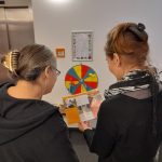 Zwei Frauen unterschiedlichen Alters studieren gemeinsam einen Flyer. Man erkennt im Hintergrund, dass sie in einer Kita sind.