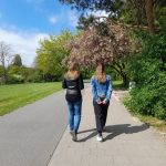 Zwei Frauen laufen durch einen Park bei Sonnenschein.